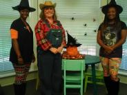Two Witches and a Scarecrow Standing by a Pumpkin